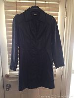 Front view of black ladies leather coat, hung against a door background, showing full length and buttons.