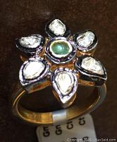Top-down view of flower-shaped ring with central green peridot cabochon and six petal diamonds on brown background