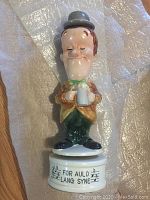 Front view of the Stan Laurel ceramic decanter with mug and musical base showing 'For Auld Lang Syne' inscription.