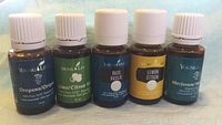Photo showing five sealed 15ml amber glass bottles of Young Living essential oils labeled Oregano, Lime, Basil, Lemon, and Marjoram.