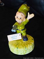 Front view of Elmer Fudd musical figure in green hunter outfit holding a shotgun, standing on grassy base with a tag from Gift World Gotham.