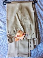 Two pairs of folded tan men's slacks with tags, showing fabric and hems