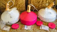 Three Bazz retro industrial ceiling lights laid out on a couch, two white shades and one pink shade, each with attached cords and canopies, plastic covers partially on the shades.