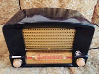 Front view of General Electric Model C600 tube radio showing the Art Deco dark glossy cabinet with curved top, gold speaker grille, and tuning dial with cream knobs.