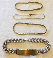 Four bracelets laid out on a white surface: one men's chrome and brass bracelet with a wide brass plate and three women's metal bracelets of varying chain styles and thicknesses.