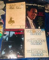 Four vintage guitar tab and lyrics books placed together on fabric background: The Best of Willie Nelson, Marvin Gaye, The Doors, and The Moody Blues.