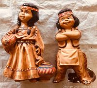 Two hand painted ceramic figurines of young Native American children and a small dog in front, posed on cloth. Both children dressed in traditional clothing with decorative patterns, showing good detail.