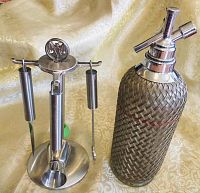 Bacardi branded stainless steel bar set stand with 4 bar tools hanging, alongside vintage wire wrapped glass seltzer bottle