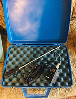 Electric wall inspection periscope laid in its blue hard case with foam padding, showing the rod, power supply, and coiled cable.