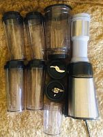 Top-down photo of blender base, blending jars, lids, two blade attachments, and a white filter attachment laid flat
