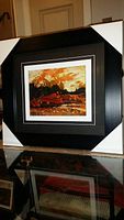 Photo showing full framed art piece with protective corner guards, black frame, and visible art print inside.