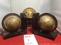 Front view showing a pair of globe bookends with antique map design and degree markings on black semi-circular frames on dark wood bases with a small vintage globe on a decorative wooden stand in the background.