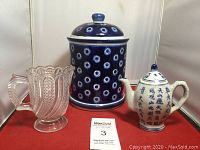 Photo of blue and white cookie jar, pink glass pitcher, and blue and white teapot grouped on a red surface