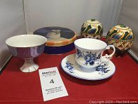 Blue-themed kitchen decor on red backdrop showing 6 items: porcelain teacup and saucer, footed bowl, decorative tin, and two egg-shaped containers