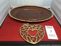 Photo of brown pottery plater with leaf design and brass trivet on red surface