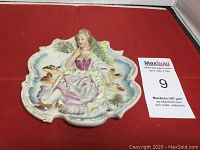 Front view of the hand painted vintage wall plaque showing a woman reclining in a natural setting with detailed sculpting and pastel colors.