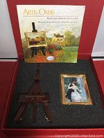 Miniature framed reproduction artwork and wooden easel in gift box with booklet behind.