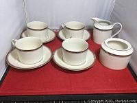 Full set showing cups, saucers, creamer, and sugar bowl arranged on a red cloth.