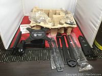 Full lot contents showing black metal swivel mount, plastic wrapped components, mounting hardware, and packaging material