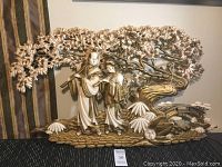 Full view of the wall hanging showing two figures in traditional Asian dress playing flutes under a tree with sculpted flowers and leaves.