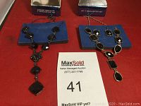 Photo showing two statement necklace sets, each with a necklace and matching earrings on blue display cards on red surface with auction card