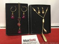 Two sets of necklaces and earrings placed in black boxes on a red surface.