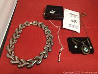 Wide view of all jewelry in the lot on a red surface including chunky chain necklace, silver chain necklace with pearls and rhinestones, and bronze-toned pendant set with earrings.