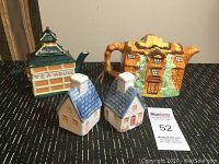 Two ceramic building-shaped teapots and two blue-roof cottage salt and pepper shakers on display.