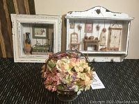 Two white wooden shadow boxes displayed side by side on a dark surface with a floral arrangement in front
