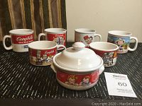 Photo of six vintage Campbell Soup mugs with various characters and logos, along with a covered sugar bowl decorated with Campbell Soup characters.