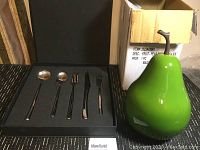 Set of stainless steel serving utensils in black case next to the large green decorative pear and cardboard box