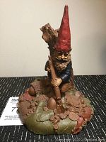 Front view of the ceramic/resin gnome figurine, showing a gnome with a red pointed hat, beard, blue jacket, and detailed base with mushrooms and other forest elements.