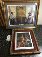 Two framed prints placed on floor, one large with golden ebony frame, one smaller with reddish ebony frame