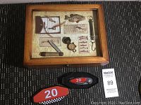 Photo of wooden fishing themed display box with pocket knife, compass, hooks, scale, and fishing info under glass.
