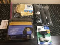Four items displayed on a black woven surface: Kevlar hose in package, two black tire pumps, Arnold starter handle in package with nylon rope