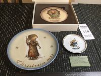 Three Goebel Hummel Christmas plates displayed on black fabric, including 1972 plate, miniature plate with green info card, and boxed plate.