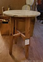 Round side table with white marble top and rustic wooden base shown indoors on wood floor, tag attached to base.