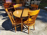 Dining table with two leafs and four country style chairs arranged around it on concrete ground outdoors.