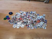 Wide view of hundreds of pogs scattered on a wooden surface along with several slammers of different colors.