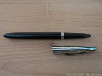 Photo of the closed fountain pen showing the black body with silver-tone band and attached silver-tone cap, placed on a wooden surface.