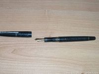 Photo of the vintage black Osmiroid fountain pen uncapped, showing the pen body and gold-tone nib on a wood surface.