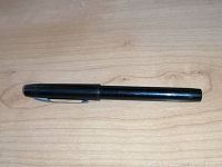 Black Parker fountain pen lying closed on a wooden surface, visible surface wear on the barrel and cap.