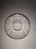 Top view of clear glass tealight holder with etched bird designs and signature.