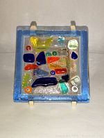 Front view of small square art glass dish showing colorful fused glass pieces and blue border.