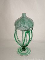 Front view of the green and white swirled glass jellyfish sculpture showing bulbous dome top, tentacle supports, and round base.