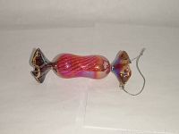 Side view of pink-red iridescent glass candy ornament showing twisted wrapped ends and hanging string.