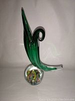 Front angle view of the green glass cornucopia vase showing its curved spout and clear base filled with colorful millefiori patterns.