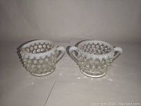 Two pieces of Fenton hobnail glass, mini sugar bowl with two handles and mini creamer with spout and handle, both white opalescent glass with hobnail pattern.