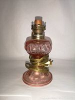 Front view of pink Depression glass converted electric travel lamp with visible brass electric socket and power cord wrapped around base.