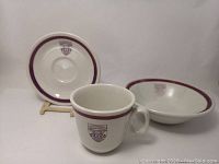 Set of three ceramic pieces including cup, saucer, and bowl, all white with purple rims and old University of Western Ontario crest